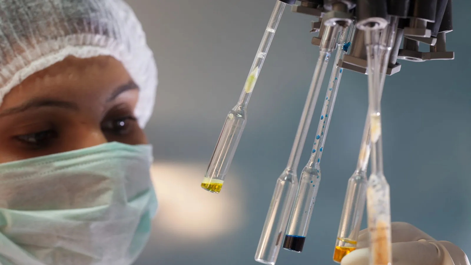 Laborantin mit Haube und Maske hält Pipetten