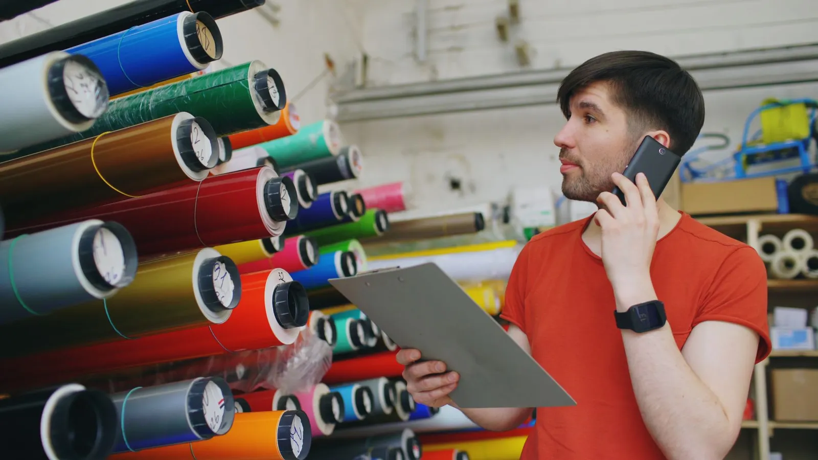 Mitarbeiter mit Klemmbrett und Telefon vor Materialrollen